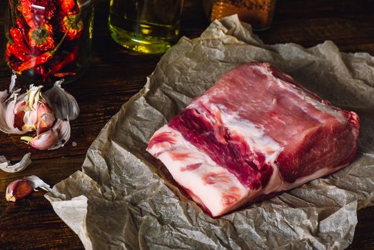 Raw pork loin on baking paper. Some ingredients on background.