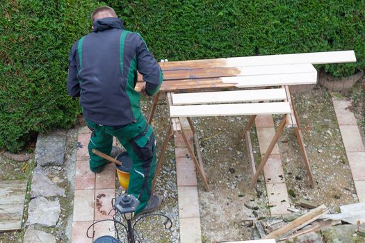 Man with a paintbrush stroking wooden beams.