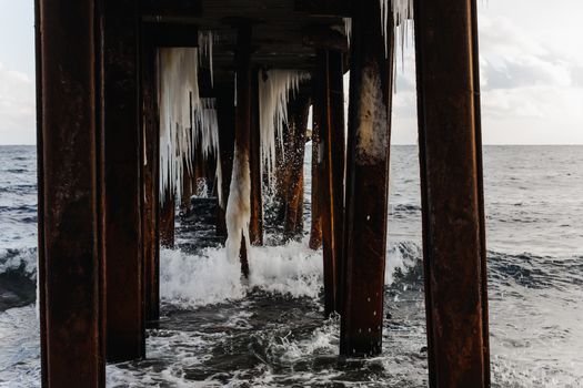 old rusty pier with icicles in the sea ocean in winter, splashing waves