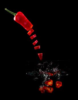 Tomato, two types of paprika and eggplant slices fall into water, on black background