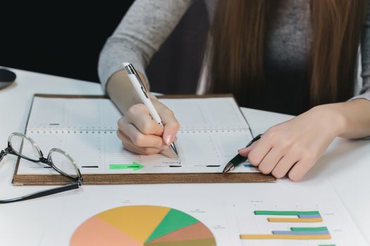 women's hands write in a calendar notepad on the table, next to them are graphs and glasses