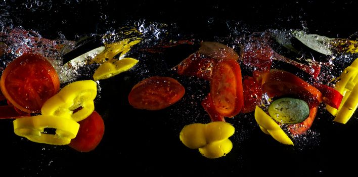 Tomato, two types of paprika and eggplant slices fall into water, on black background