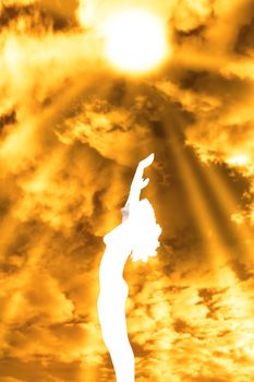 attractive silhouetted nude woman holding her hands up to the sky giving gratitude to the heavens in a yoga pose with a cloudy background