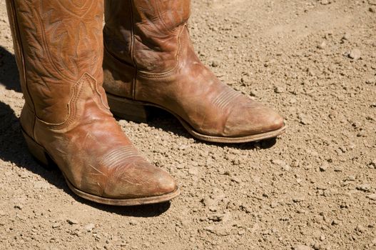 Two dirty western cowboy boots standing on dry dirt