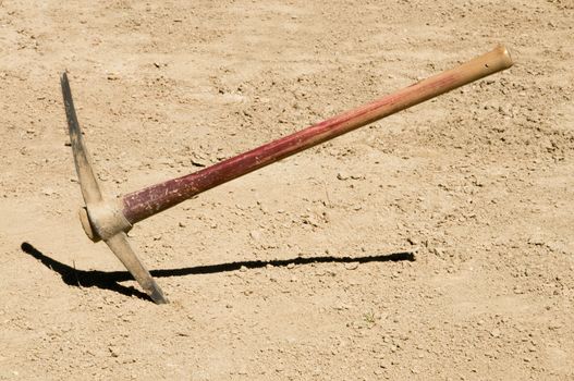 Worn distressed pick ax plunged into dirt ground