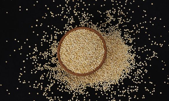 Quinoa seeds. Wooden bowl of healthy white quinoa grains isolated on black background, close-up, top view