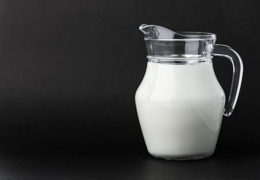 Glass jug of fresh milk on black background with copy space, pitcher of cream