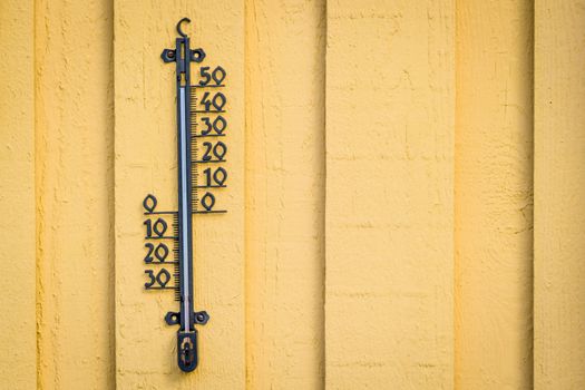 Weather thermometer hanging on a yellow wall on wooden planks