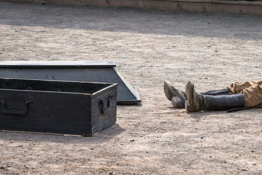 Coffin next to a dead man with his boots on a dirt road in a wild west city