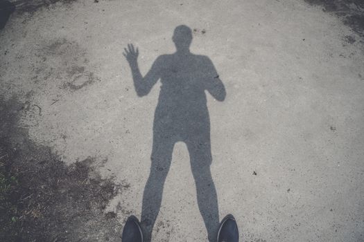 Male shadow on the ground waving hello with one hand