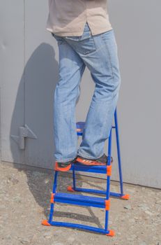 The man in the blue jeans standing on a ladder outdoors.