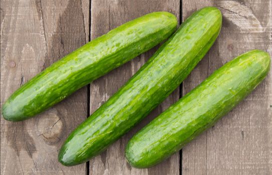 Fresh cucumbers on old wooden background, top view.