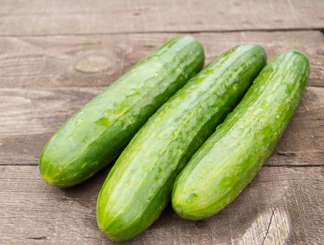 Three fresh cucumber lying on an old wooden background.