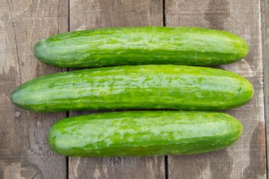 Fresh cucumbers on old wooden background, top view.