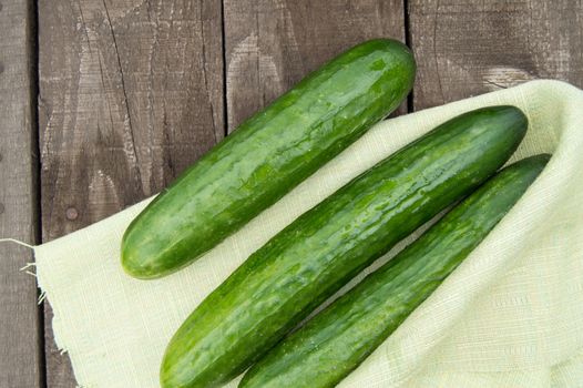 Cucumbers are lying on an old wooden background with napkin.