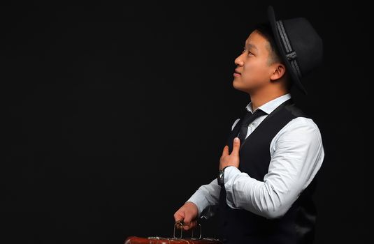 Asian man in a black hat turned aside, looking sideways on a black background