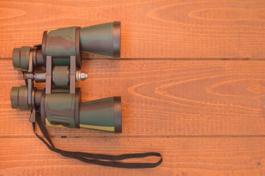 Binoculars protective khaki on wooden background, top view.