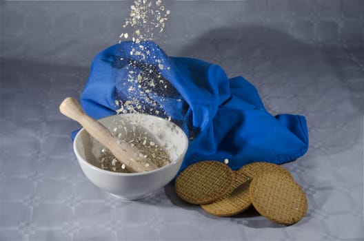 Oat flakes falling on a ceramic bowl and cookies on a neutral background