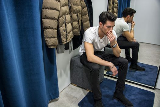 Young Handsome Man Trying on Clothes in Clothing Store's Changing Room in Front of a Mirror or in Room Closet