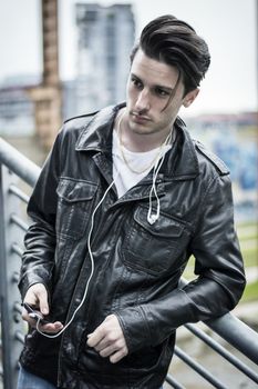 Handsome young man standing outdoors in urban environment on metal stairs, looking at camera