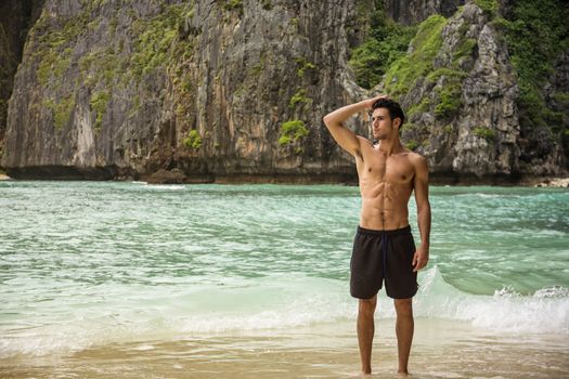 Half body shot of a handsome young man standing on a beach in Phuket Island, Thailand, shirtless wearing boxer shorts, showing muscular fit body