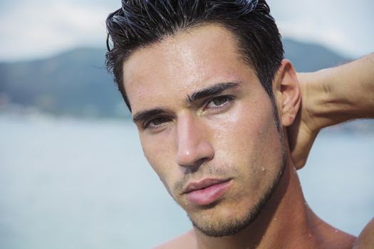 Attractive young man in the sea getting out of water with wet hair, looking in camera