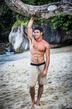 Half body shot of a handsome young man standing on a beach in Phuket Island, Thailand, shirtless wearing boxer shorts, showing muscular fit body