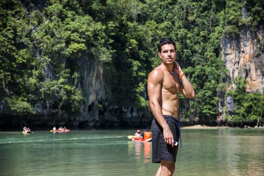 Half body shot of a handsome young man standing on a beach in Phuket Island, Thailand, shirtless wearing boxer shorts, showing muscular fit body