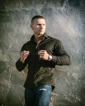 One handsome young man in urban setting in European city, standing, wearing black jacket and jeans