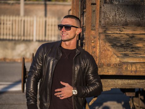 One handsome young man in urban setting in European city, standing, wearing black leather jacket and jeans