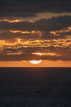 Sun nearly touching the horizon partly covered by red shining clouds at Indian Ocean