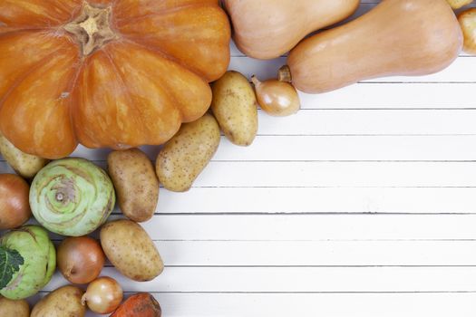 Autumn vegetables on white wooden table background. Pumpkin, zucchini, potatoes, onions, top view