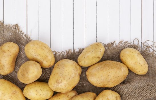 Raw potato, pile of potatoes on burlap bag over white wooden table background, top view