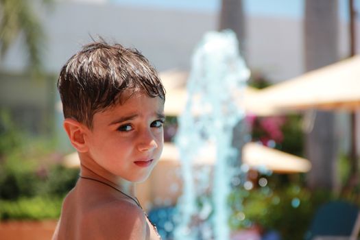 Little boy on the blurred background of a swimming pool with a fountain on holiday in a hotel on a sunny summer day.