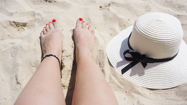 Summer holiday fashion concept - tanning woman legs and sun hat at the beach on a white sand