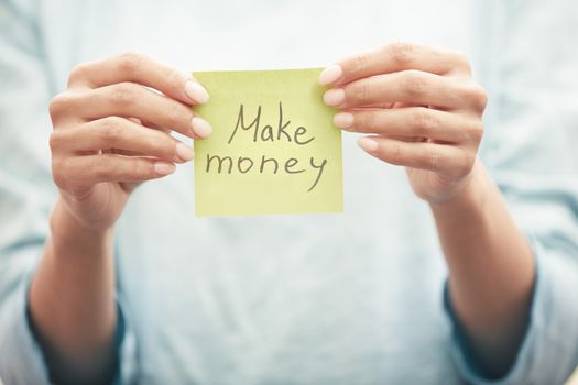 Woman holding sticky note with Make money text
