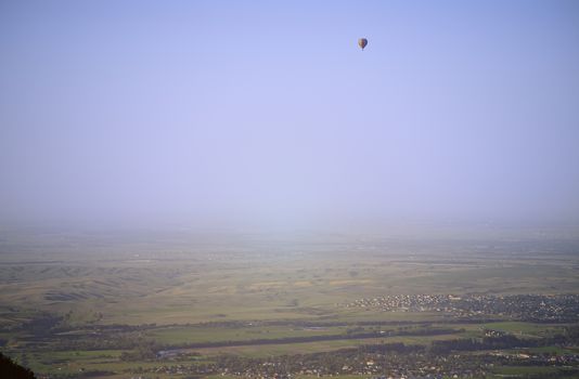 Hot air balloon above the green field and villages