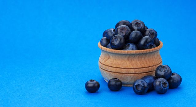 Blueberry isolated on blue background with copy space. A pile of fresh blueberries in a wooden bowl, fresh wild berries, healthy food concept, close-up