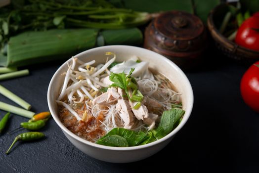 Asian rice noodles soup and chicken in bowl on dark background.
