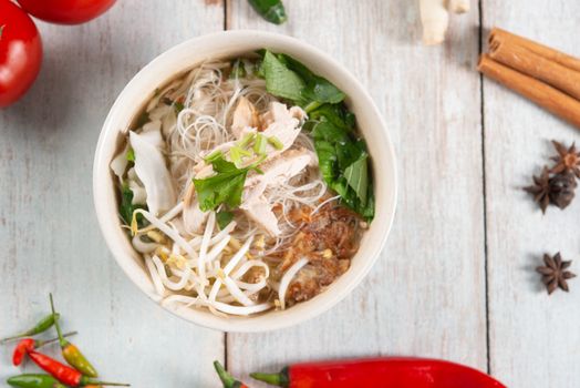 Asian rice noodles soup with vegetables and chicken in bowl. Top view flat lay on wooden background.