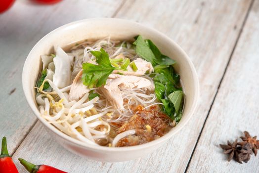 Asian rice noodles soup with vegetables and chicken in bowl on wooden background.