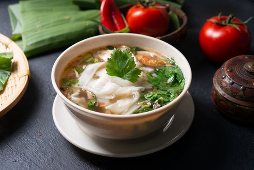 Asian kway teow soup noodle and chicken in bowl on dark background. 