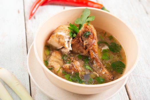 Asian style chicken soup in bowl, wooden background. 