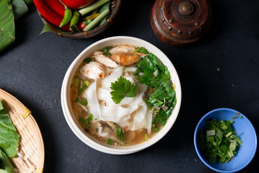 Asian kway teow soup noodles and chicken in bowl on dark background. Top view flat lay.