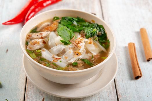 Asian kway teow soup noodle and chicken in bowl on wooden background. 