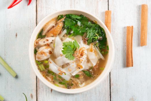 Asian kway teow soup noodles and chicken in bowl on wooden background. Top view flat lay.