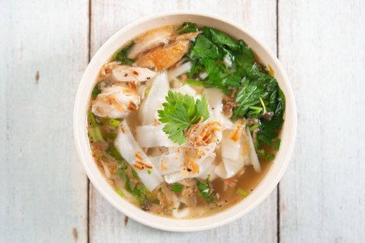 Asian kway teow soup noodles and chicken in bowl on wooden background. Top view flat lay.