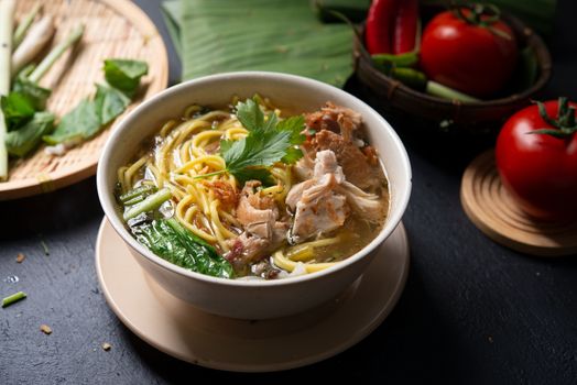 Asian soup noodles and chicken in bowl on dark background. 
