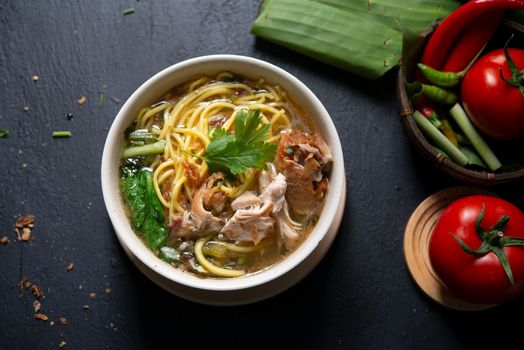 Asian soup noodles and chicken in bowl on dark background. Top view flat lay.