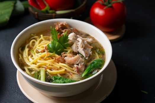 Asian soup noodles and chicken in bowl on dark background. 